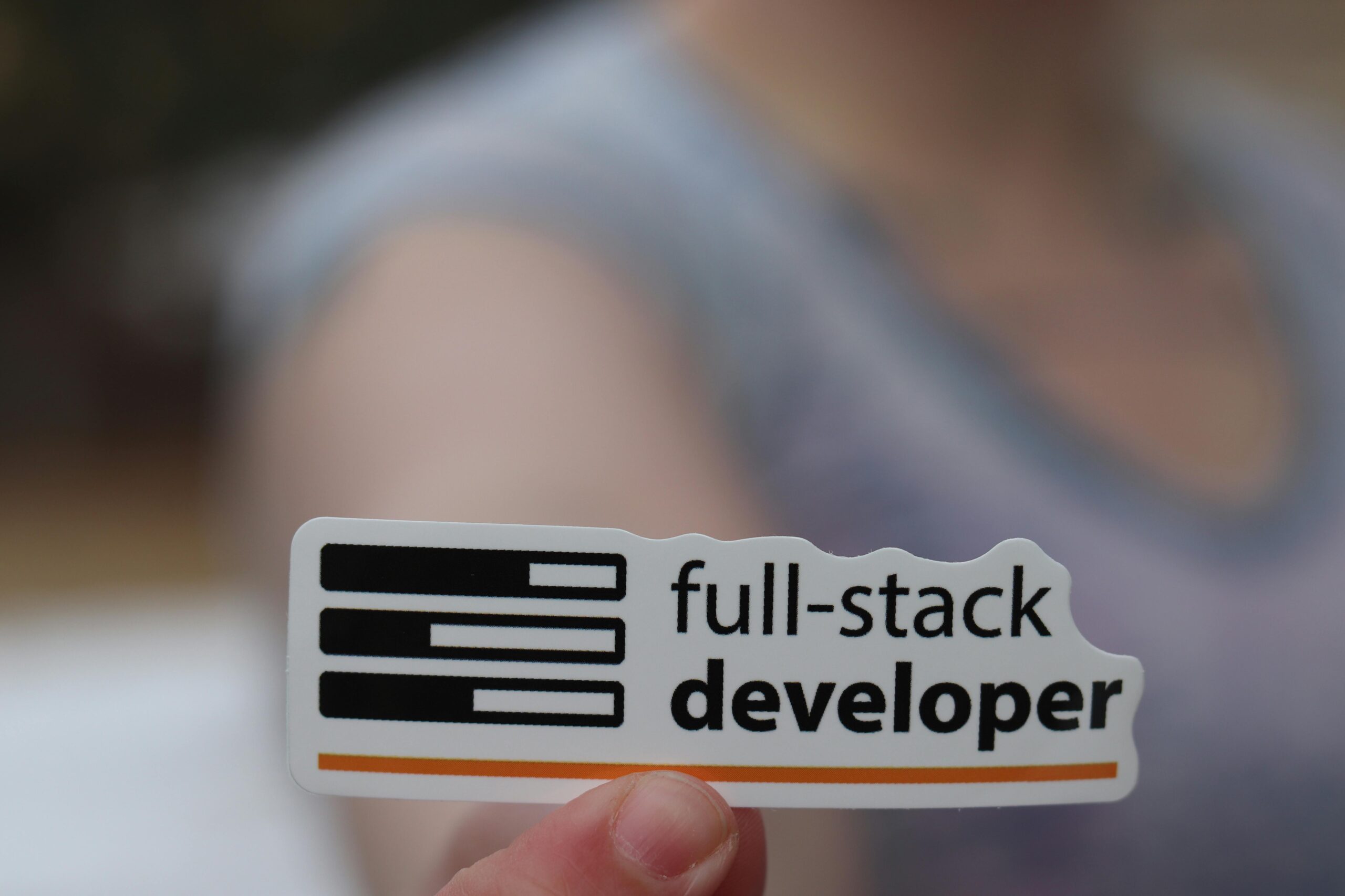 A hand holding a sticker labeled 'full-stack developer', symbolizing technology and programming skills.