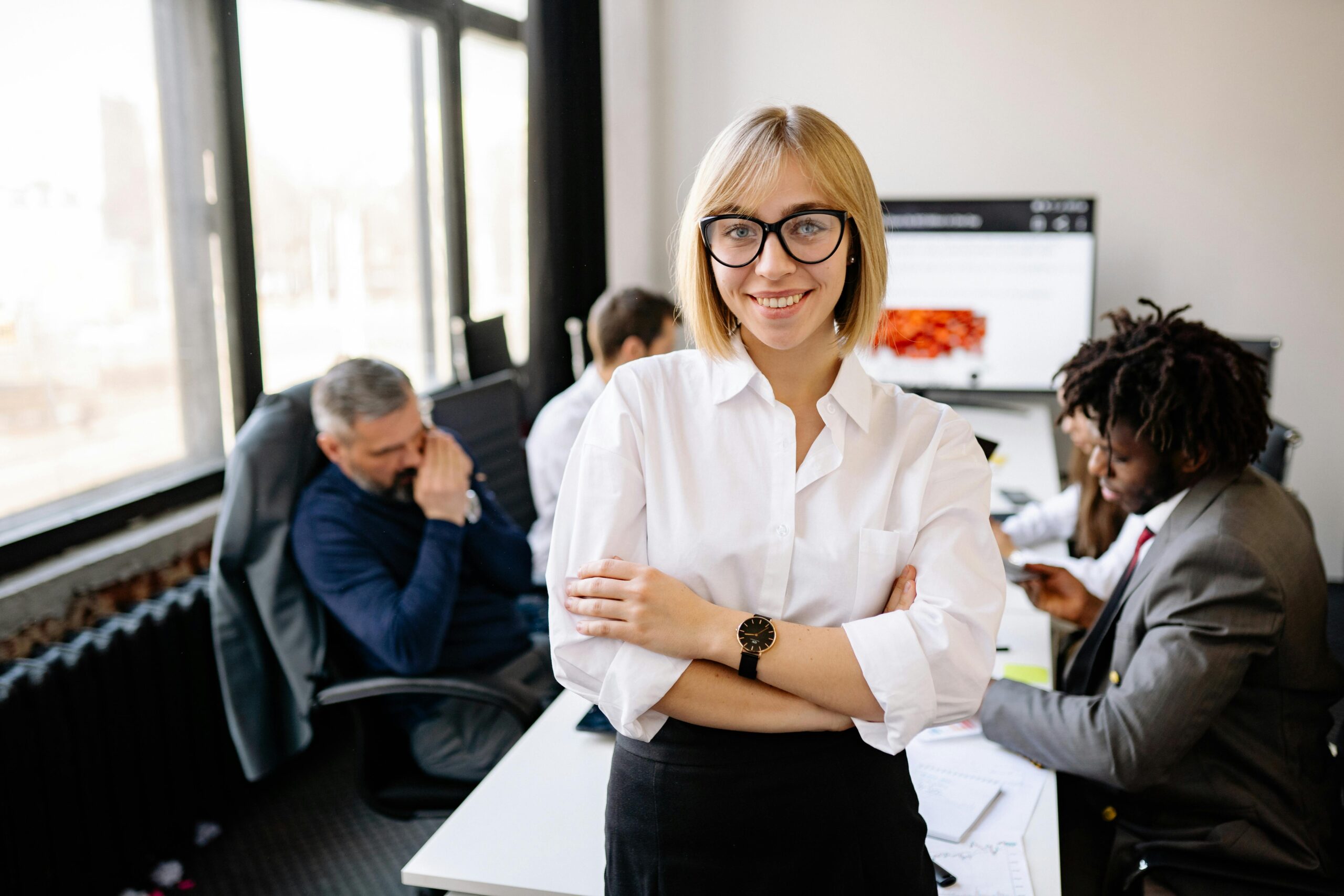 Smiling businesswoman in white shirt guiding her team in a modern office environment.